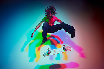 Image showing Skateboarder doing a trick isolated on studio background in colorful neon light