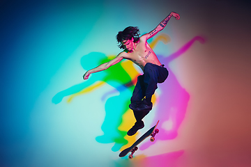 Image showing Skateboarder doing a trick isolated on studio background in colorful neon light