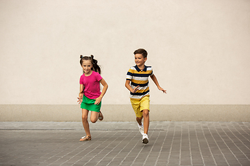 Image showing Two smiling kids, boy and girl running together in town, city in summer day