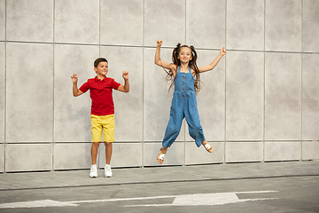 Image showing Two smiling kids, boy and girl jumping together in town, city in summer day