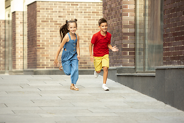 Image showing Two smiling kids, boy and girl running together in town, city in summer day