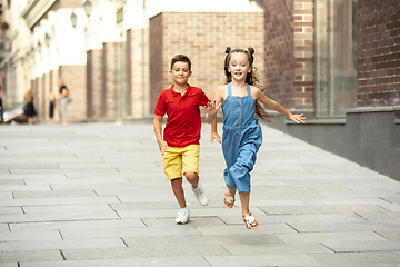 Image showing Two smiling kids, boy and girl running together in town, city in summer day