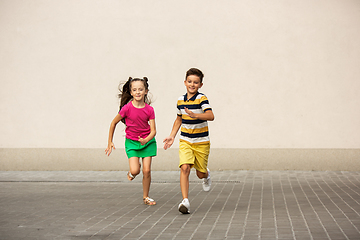 Image showing Two smiling kids, boy and girl running together in town, city in summer day