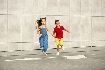 Image showing Two smiling kids, boy and girl running together in town, city in summer day