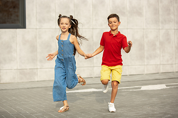 Image showing Two smiling kids, boy and girl running together in town, city in summer day