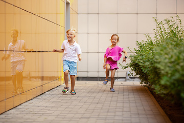 Image showing Two smiling kids, boy and girl running together in town, city in summer day