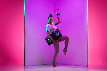 Image showing Young caucasian female musician in headphones performing on purple background in neon light