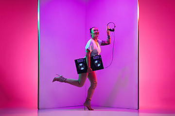 Image showing Young caucasian female musician in headphones performing on purple background in neon light