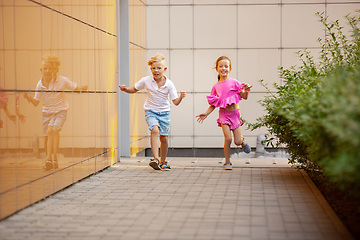 Image showing Two smiling kids, boy and girl running together in town, city in summer day