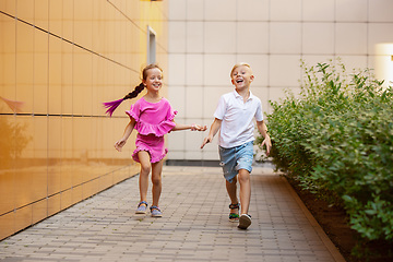 Image showing Two smiling kids, boy and girl running together in town, city in summer day