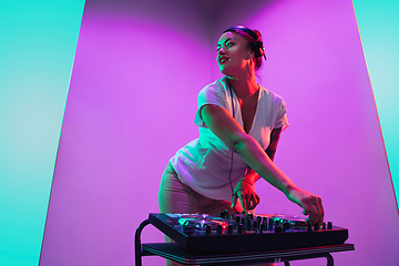 Image showing Young caucasian female musician in headphones performing on purple background in neon light