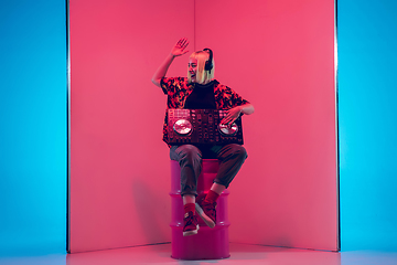 Image showing Young caucasian female musician in headphones performing on blue-red background in neon light