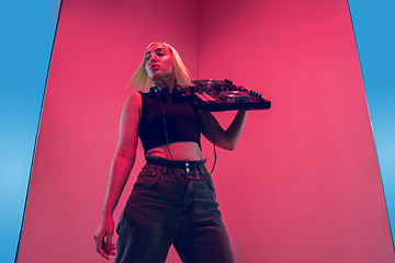 Image showing Young caucasian female musician in headphones performing on blue-red background in neon light