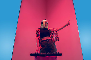 Image showing Young caucasian female musician in headphones performing on blue-red background in neon light