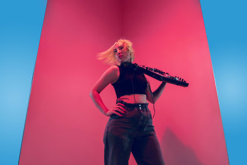 Image showing Young caucasian female musician in headphones performing on blue-red background in neon light