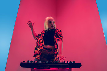 Image showing Young caucasian female musician in headphones performing on blue-red background in neon light