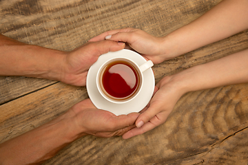 Image showing Hands of couple holding mug of tea, top view on wooden background with copyspace