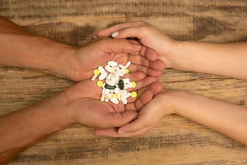 Image showing Human hands holding bunch of pills isolated on wooden background with copyspace