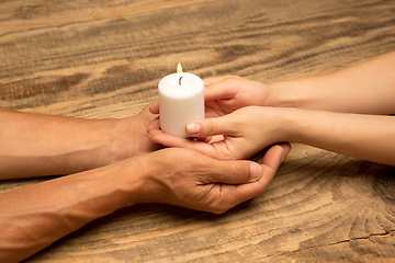 Image showing Hands guarding, holding a white candle on wooden background with copyspace