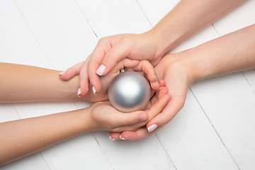 Image showing Human\'s hand holding a Christmas ball isolated on wooden white background