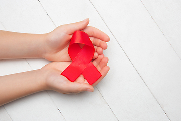 Image showing Female and male hands holding red HIV and AIDS awareness ribbon isolated on wooden background
