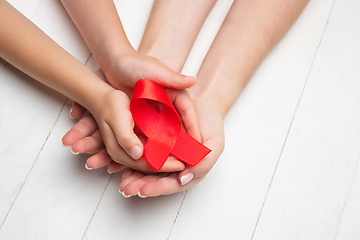 Image showing Female and male hands holding red HIV and AIDS awareness ribbon isolated on wooden background