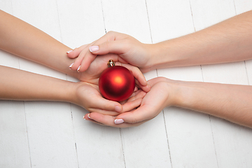 Image showing Human\'s hand holding a Christmas ball isolated on wooden white background