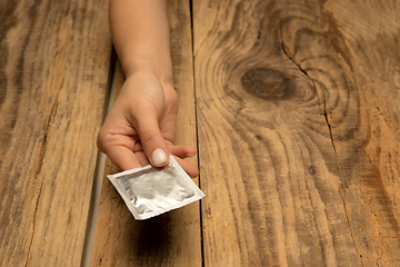 Image showing Female hand holding condom isolated on wooden background