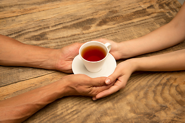 Image showing Hands of couple holding mug of tea, top view on wooden background with copyspace