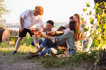 Image showing Group of friends clinking beer glasses during picnic at the beach. Lifestyle, friendship, having fun, weekend and resting concept.