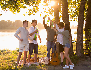 Image showing Group of friends clinking beer bottles during picnic at the beach. Lifestyle, friendship, having fun, weekend and resting concept.