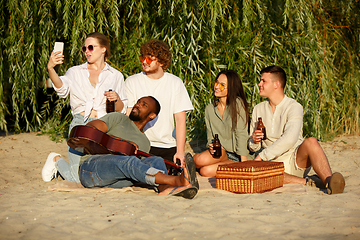 Image showing Group of friends clinking beer glasses during picnic at the beach. Lifestyle, friendship, having fun, weekend and resting concept.