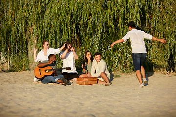 Image showing Group of friends clinking beer glasses during picnic at the beach. Lifestyle, friendship, having fun, weekend and resting concept.