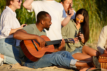 Image showing Group of friends clinking beer glasses during picnic at the beach. Lifestyle, friendship, having fun, weekend and resting concept.