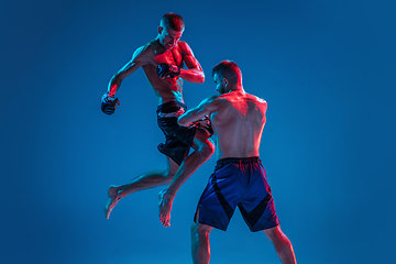 Image showing MMA. Two professional fighters punching or boxing isolated on blue studio background in neon