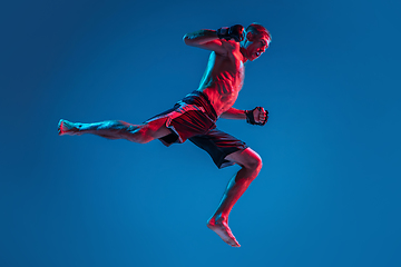 Image showing MMA. Professional fighter punching or boxing isolated on blue studio background in neon