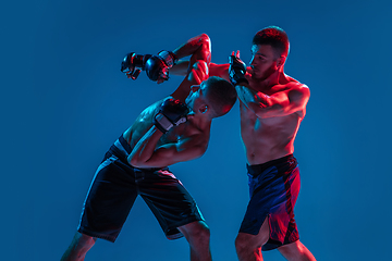 Image showing MMA. Two professional fighters punching or boxing isolated on blue studio background in neon