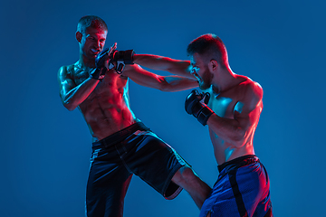 Image showing MMA. Two professional fighters punching or boxing isolated on blue studio background in neon