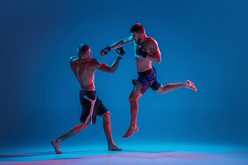 Image showing MMA. Two professional fighters punching or boxing isolated on blue studio background in neon