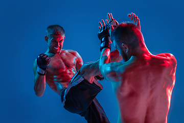 Image showing MMA. Two professional fighters punching or boxing isolated on blue studio background in neon