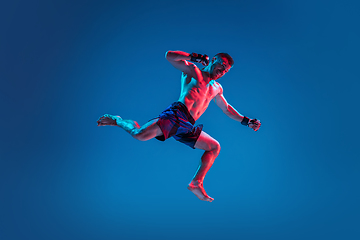 Image showing MMA. Professional fighter punching or boxing isolated on blue studio background in neon