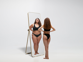 Image showing Young fit, slim woman looking at fat girl in mirror\'s reflection on white background