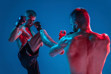 Image showing MMA. Two professional fighters punching or boxing isolated on blue studio background in neon