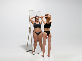 Image showing Young fit, slim woman looking at fat girl in mirror\'s reflection on white background