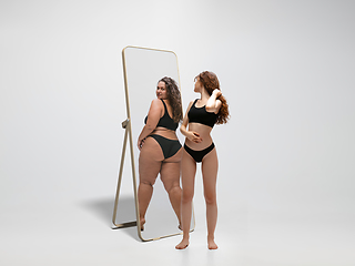 Image showing Young fit, slim woman looking at fat girl in mirror\'s reflection on white background