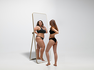 Image showing Young fit, slim woman looking at fat girl in mirror\'s reflection on white background