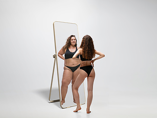 Image showing Young fit, slim woman looking at fat girl in mirror\'s reflection on white background