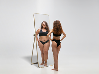 Image showing Young fit, slim woman looking at fat girl in mirror\'s reflection on white background