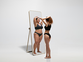 Image showing Young fit, slim woman looking at fat girl in mirror\'s reflection on white background