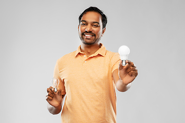 Image showing smiling indian man comparing different light bulbs